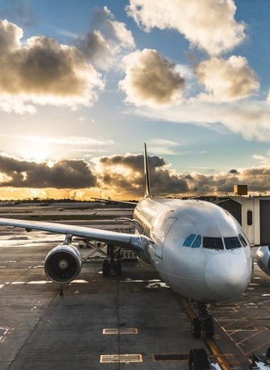 Airplane boarding passengers at airport at sunset. Long haul flight aircraft ready to leave from gate. Dramatic sky with clouds at sunset. Travel and transportation concepts